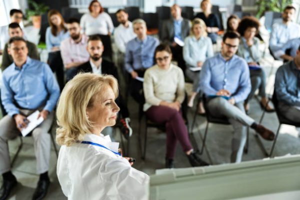 Profile view of smiling mature doctor educating large group of people about medicine in a board room.