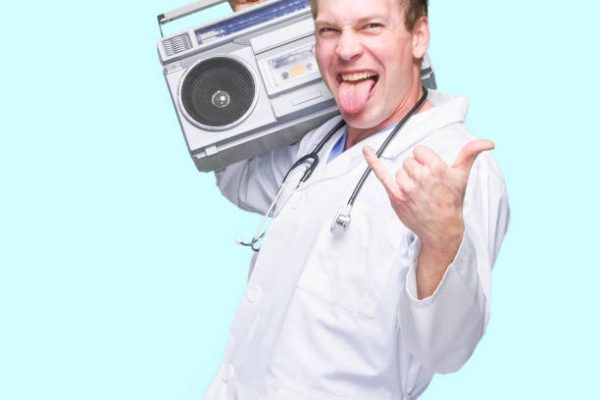 One person of with brown hair caucasian young male doctor dancing in front of colored background wearing lab coat who is listening and holding boom box